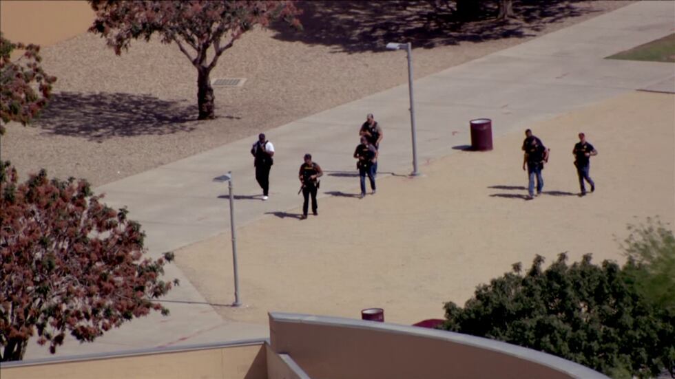 Several officers in bulletproof vests and armed with firearms are patrolling school grounds.