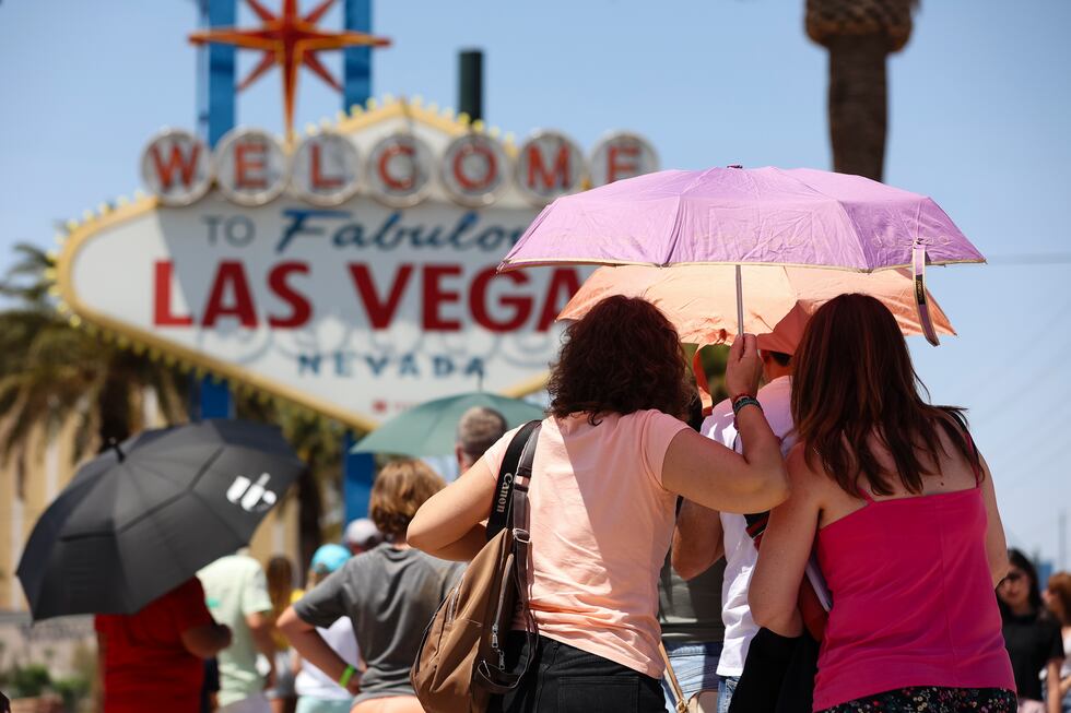 FILE - People use umbrellas to block the sun while waiting to take a photo at the "Welcome to...