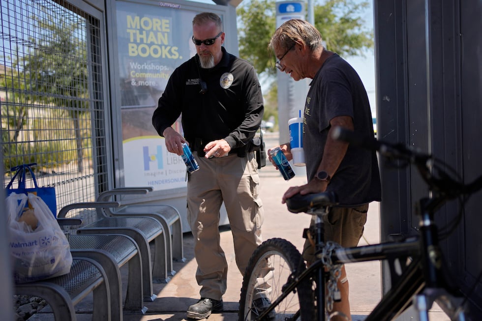 Mark Paulson, a Public Response and Code Enforcement officer, gives cans of cold water to...