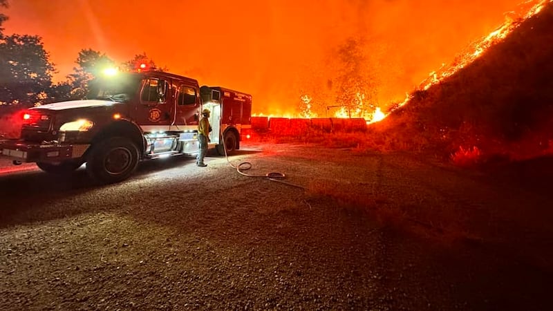 Massive orange flames burn in the background as a firefighter from flagstaff fire department...