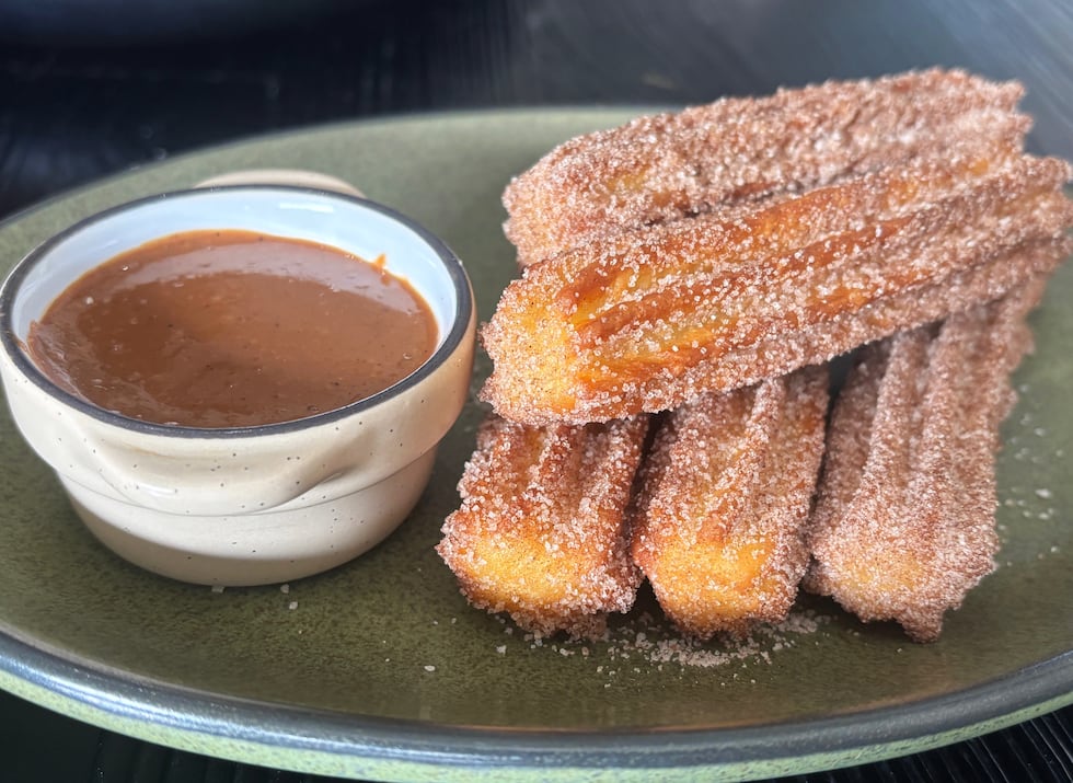 Five mini churros are dusted with cinnamon and sugar and served with a rich chocolate sauce.